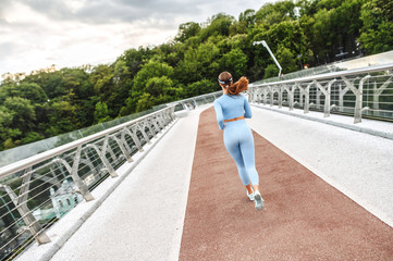 Back view of athletic woman running on the city bridge. Morning jogging. Healthy lifestyle concept