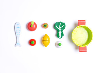 Vegetables, pot and fish toys made from wooden for kids to play on top of white background