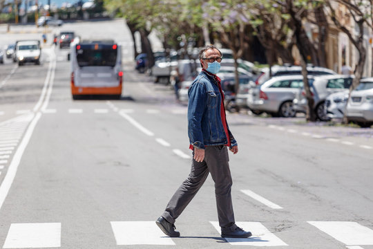 Uomo con mascherina chirurgica attraversa la strada sulle strisce pedonali in citt&agrave;
