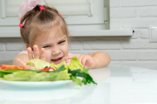 a little girl emotionally pushes away a plate of offered vegetables. children refuse vegetables in favor of junk food
