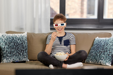 Obraz premium people and childhood concept - happy smiling boy in 3d movie glasses eating popcorn and watching tv at home