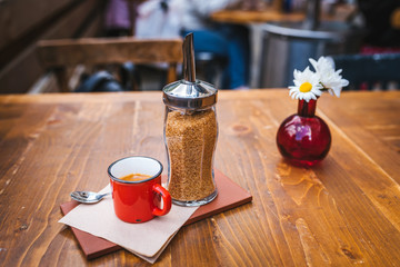 Outdoor cafe table with an espresso in a mug on the table and flower decoration on the background.