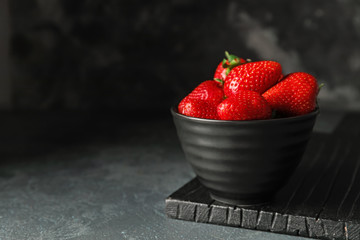 Bowl with ripe strawberry on dark background