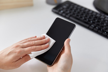 hygiene and disinfection concept - close up of woman hands cleaning smartphone with tissue