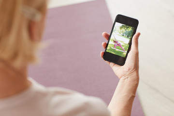 Woman holding mobile phone in her hand and watching yoga online at home