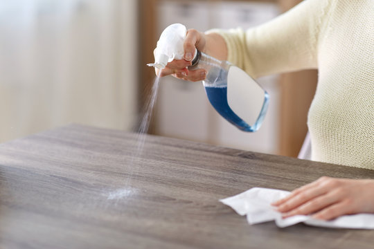 house cleaning, hygiene and disinfection concept - close up of woman or housewife with spray detergent and paper tissue wiping table at home