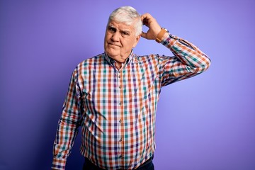 Senior handsome hoary man wearing casual colorful shirt over isolated purple background confuse and...