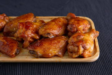 Baked chicken wings in a wooden dish on a dark cloth.
