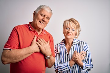 Senior beautiful couple standing together over isolated white background smiling with hands on chest with closed eyes and grateful gesture on face. Health concept.