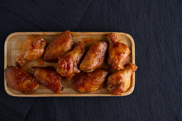 Baked chicken wings in a wooden dish on a dark cloth.