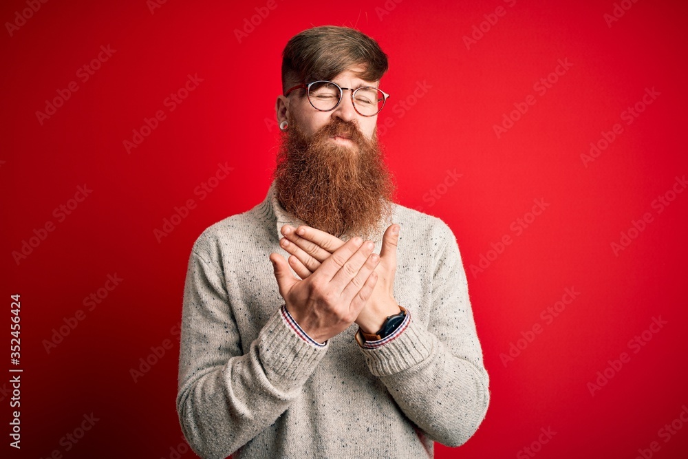 Poster handsome irish redhead man with beard wearing casual sweater and glasses over red background sufferi