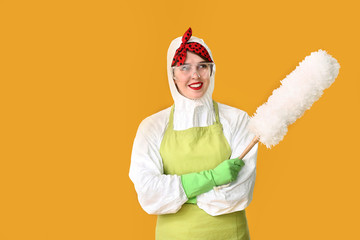 Fototapeta na wymiar Housewife in protective costume and with dust brush on color background