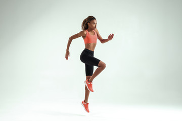 Fototapeta na wymiar Higher and higher. Side view of young african woman with perfect body in sports clothing jumping while training in studio