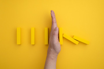 a yellow domino block that begins to fall and a hand that prevents it from falling.