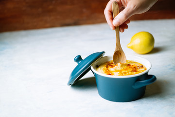 A woman's hand holding a wooden spoon to eat a delicious hummus with olive oil and paprika and lemon put on a wooden white background. food concept