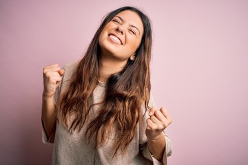 Young beautiful brunette woman wearing casual sweater standing over pink background very happy and...