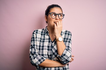 Young beautiful brunette woman wearing casual shirt and glasses over pink background looking...