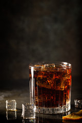 Glass of cold cola with ice cubes on dark background