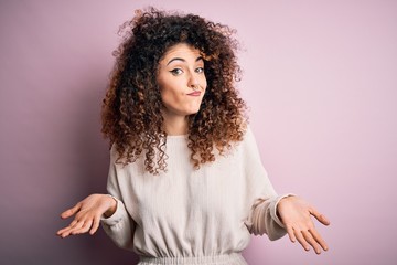 Beautiful woman with curly hair and piercing wearing casual sweater over pink background clueless...