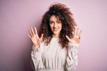 Beautiful woman with curly hair and piercing wearing casual sweater over pink background showing...
