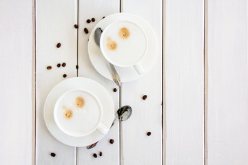 Two cups of coffee are on the table with coffee beans.