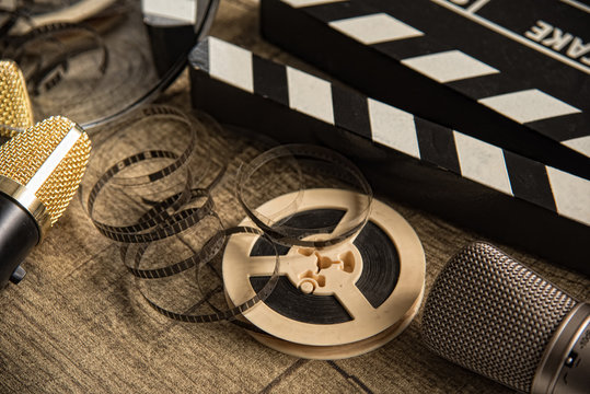 Film reel, movie clapperboard and two microphones on a table with