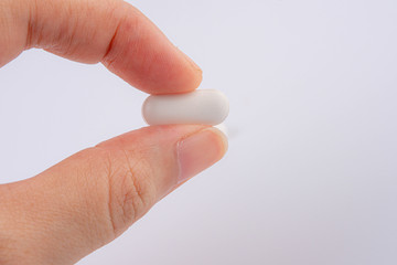 Hand holding a pill between thumb and forefinger isolated on white background.Close-up