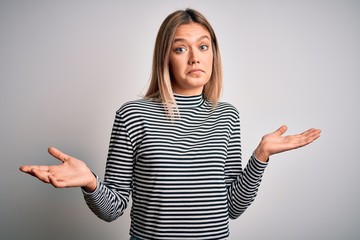 Young beautiful blonde woman wearing casual striped sweater over isolated background clueless and...
