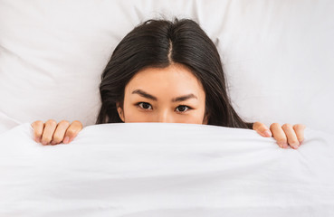 Asian Woman Peeking Out Of Blanket Waking Up In Bed