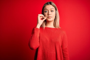 Young beautiful blonde woman wearing casual sweater over red isolated background mouth and lips shut as zip with fingers. Secret and silent, taboo talking