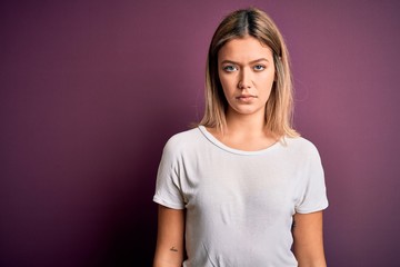 Obraz premium Young beautiful blonde woman wearing casual white t-shirt over purple isolated background with serious expression on face. Simple and natural looking at the camera.