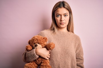 Young beautiful woman holding teddy bear standing over isolated pink background with a confident expression on smart face thinking serious