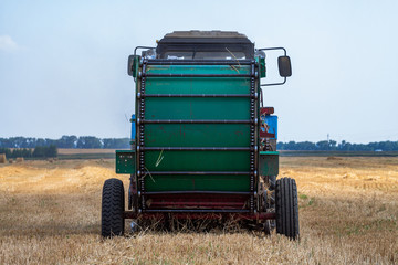 tractor makes big straw roll on yellow field at summer day