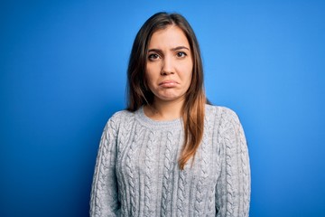 Beautiful young woman wearing casual wool sweater standing over blue isolated background depressed and worry for distress, crying angry and afraid. Sad expression.