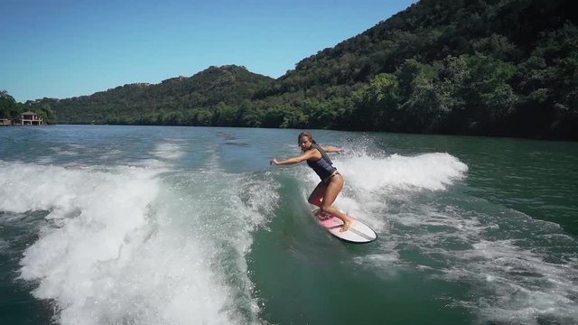 Female wake surfer landing big air grab in slow motion while wake surfing on Lake, Austin Texas