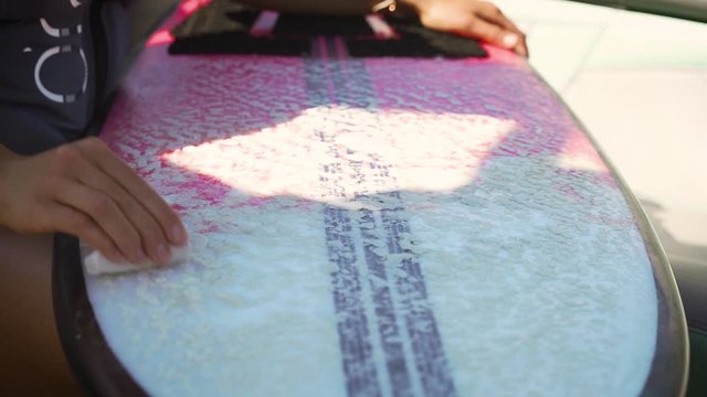 Female hand waxing pink and white wake surf surfboard in preparation for water sports