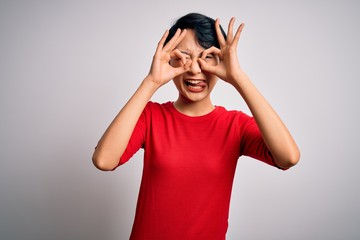Obraz na płótnie Canvas Young beautiful asian girl wearing casual red t-shirt standing over isolated white background doing ok gesture like binoculars sticking tongue out, eyes looking through fingers. Crazy expression.