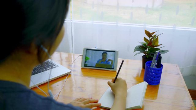 A young Asian woman is sitting down to take notes while meeting online via Smart Device.