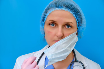 A doctor with wounds on his face takes off a medical mask. Nurse on a blue background with mask marks, closeup