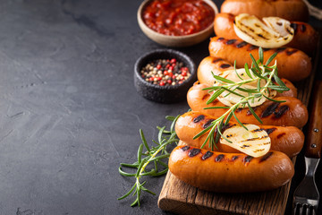 Fried delicious sausages with tomato sauce and herbs on cutting board, black background.