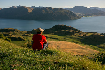 Rear view of a man sitting on top of a Summit Views on Roys Peak. Wanaka, Southern Alps, New...