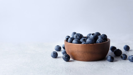 Heap of fresh blueberries in a wooden bowl with soft plain blue background