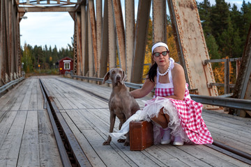 Obraz premium Hübsche Frau mit einem Weimaraner Jagdhund und Koffer auf einer alten Brücke mit Schienen