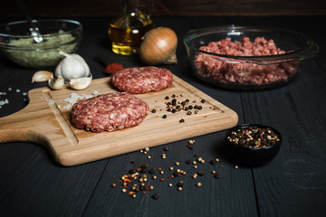 Raw cutlets with ingredients on a black wooden table.