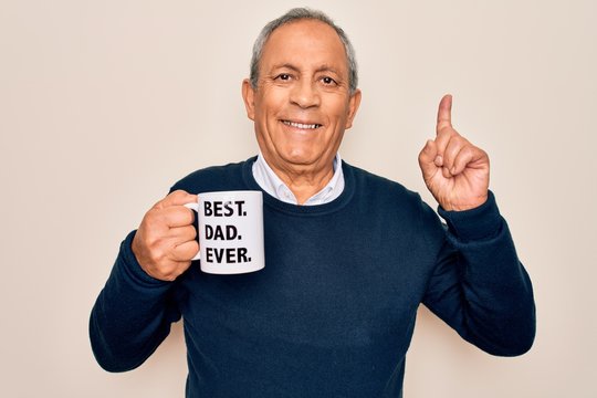 Senior man drinking cup of coffee with best dad ever message over white background surprised with an idea or question pointing finger with happy face, number one