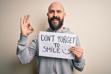 Handsome bald man with beard holding banner with funny positive message doing ok sign with fingers, excellent symbol