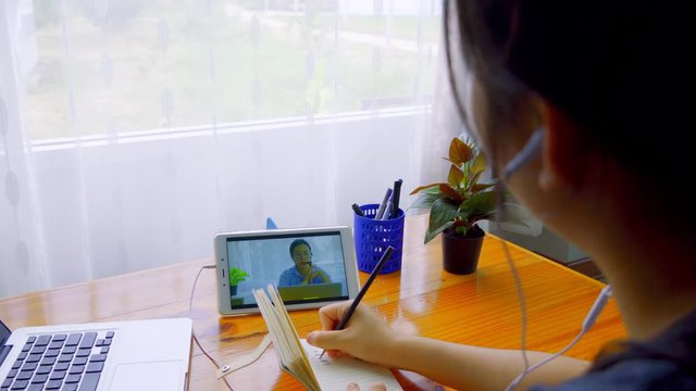 A young Asian woman is sitting down to take notes while meeting online via Smart Device.