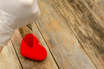 Woman's hand in white gloves with a knife pierces a red heart on a wooden background, copy space.