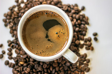 Top view of black coffee in white cup, with roasted fresh beans around. Coffee cup and coffee beans on white background. Black coffee in a coffee cup top view isolated on white background.