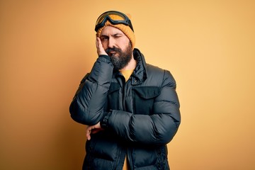 Handsome skier bald man with beard skiing wearing snow sportswear and ski goggles thinking looking tired and bored with depression problems with crossed arms.